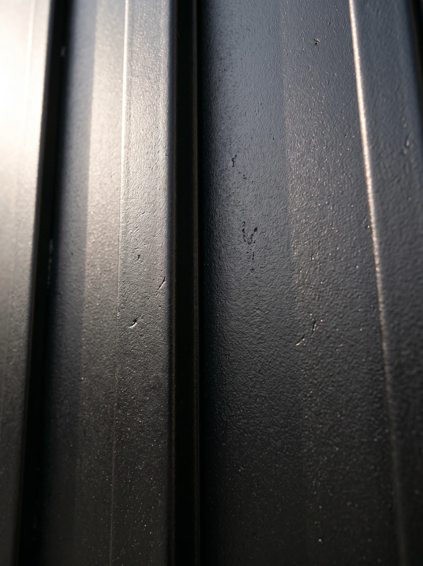 A close-up of a black steel surface with a vertical ribbed texture, side-lit